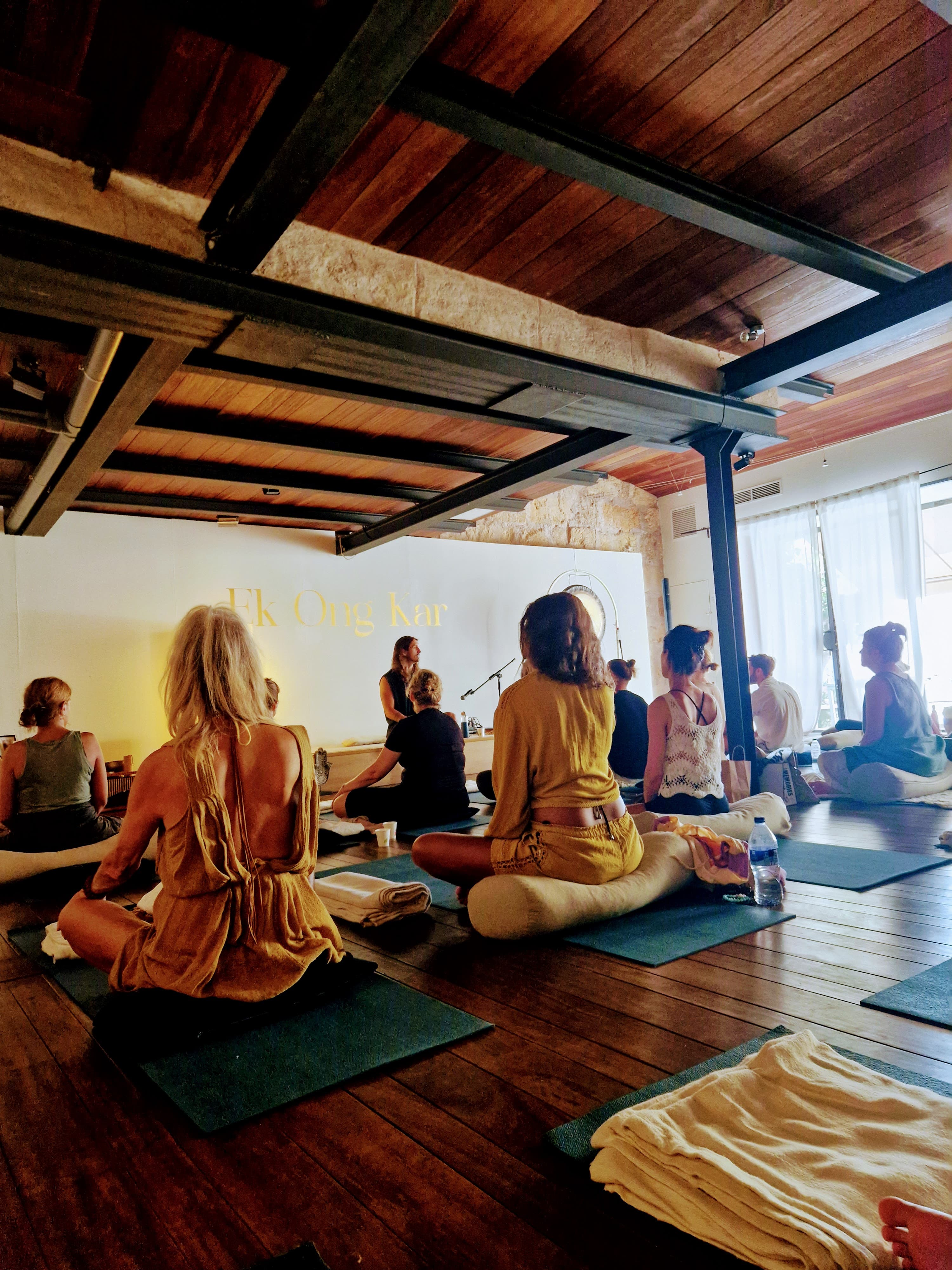 People sit on yoga mats in a studio with a wooden ceiling during meditation.