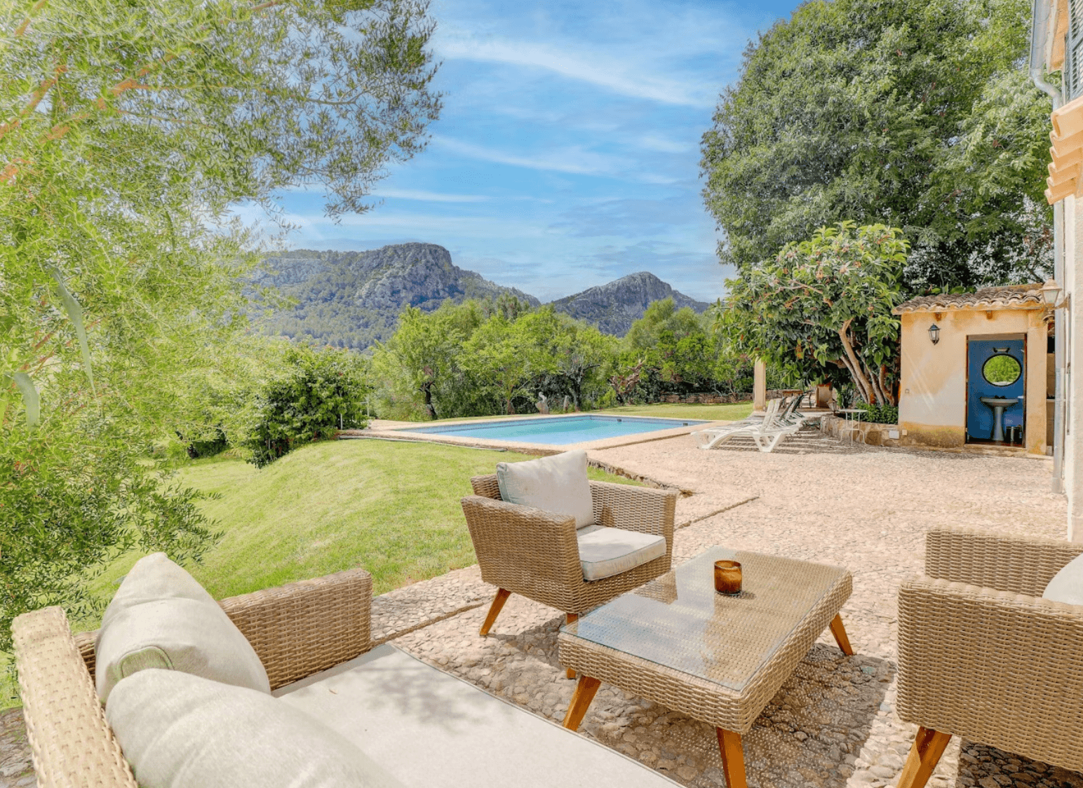 Outdoor wicker furniture on a stone patio overlooking a swimming pool and scenic mountains.